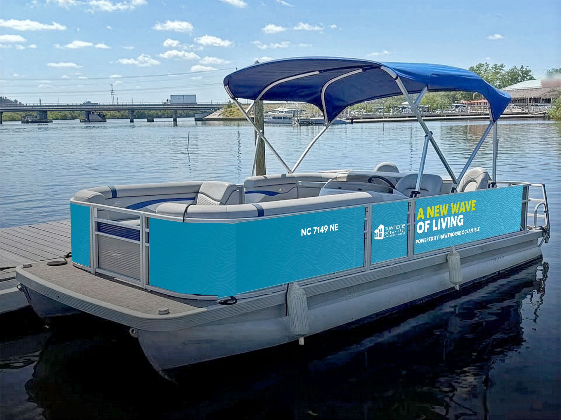 A blue pontoon boat with a canopy floats on water near a dock on a sunny day.