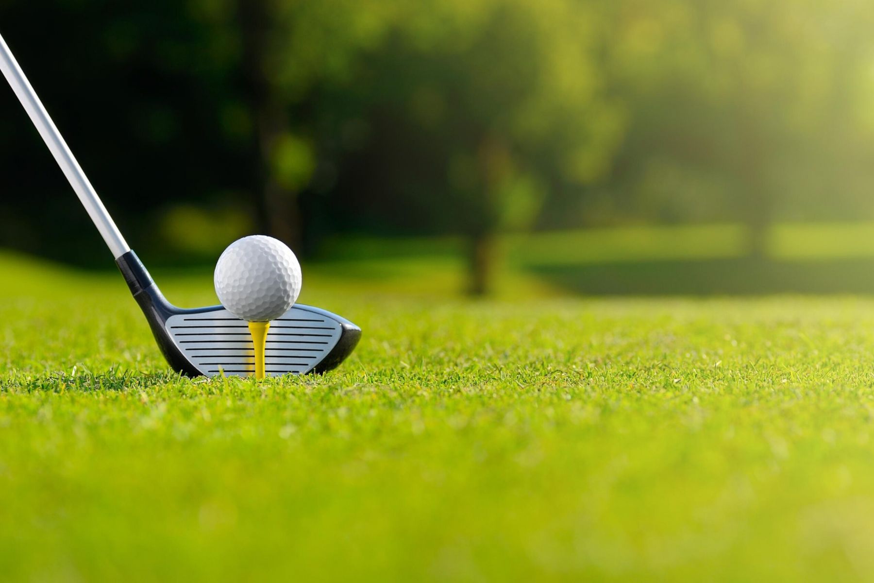 Close-up of a golf club and golf ball on a tee, ready for a shot on a sunny golf course.